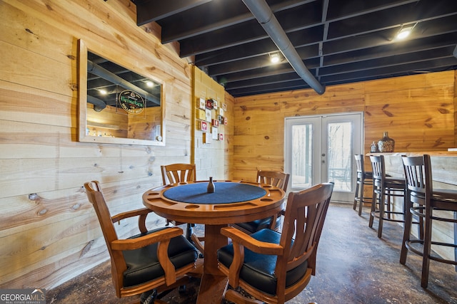 dining room with concrete floors, french doors, beamed ceiling, and wooden walls