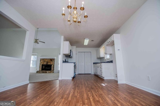 interior space with baseboards, dark wood finished floors, a ceiling fan, and a stone fireplace