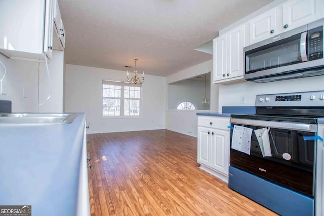 kitchen featuring light wood finished floors, a chandelier, appliances with stainless steel finishes, white cabinetry, and a sink