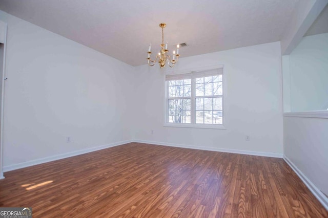 spare room with a notable chandelier, wood finished floors, and baseboards