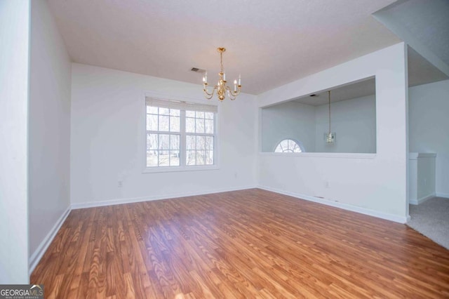 unfurnished room with a chandelier, wood finished floors, visible vents, and baseboards