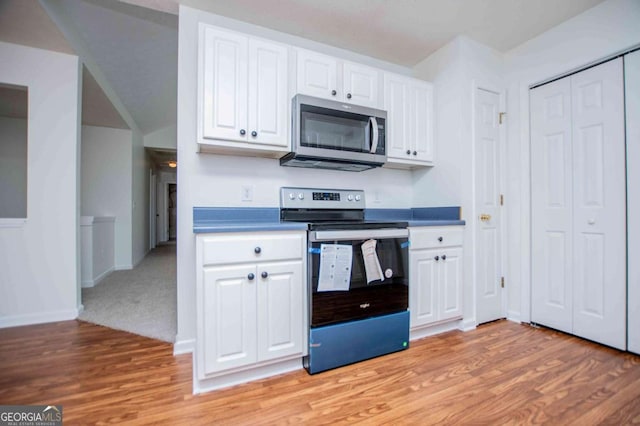 kitchen with appliances with stainless steel finishes, white cabinets, light wood-style floors, and baseboards