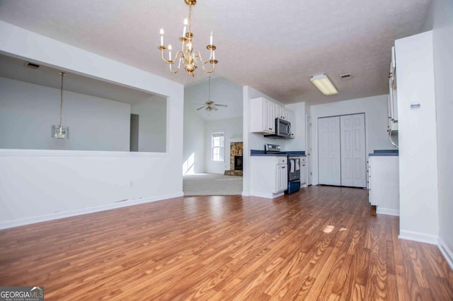 unfurnished living room featuring a stone fireplace, ceiling fan with notable chandelier, wood finished floors, baseboards, and vaulted ceiling