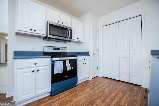 kitchen with appliances with stainless steel finishes, dark wood-type flooring, dark countertops, and white cabinetry