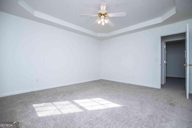 carpeted spare room with a ceiling fan, a tray ceiling, and baseboards