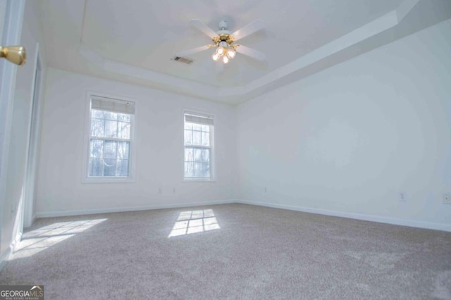 empty room with carpet, visible vents, a tray ceiling, and a ceiling fan