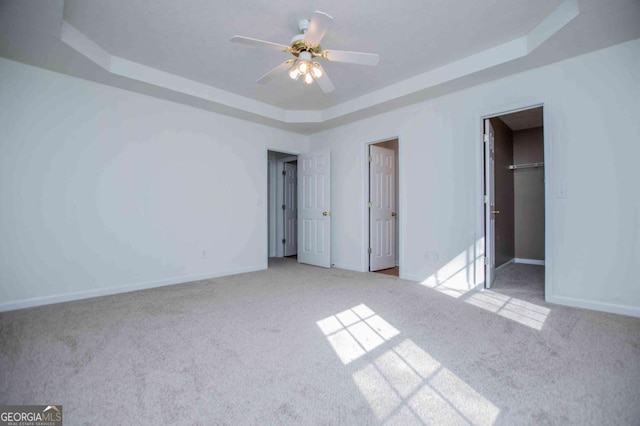 unfurnished bedroom featuring carpet floors, baseboards, a raised ceiling, and a walk in closet