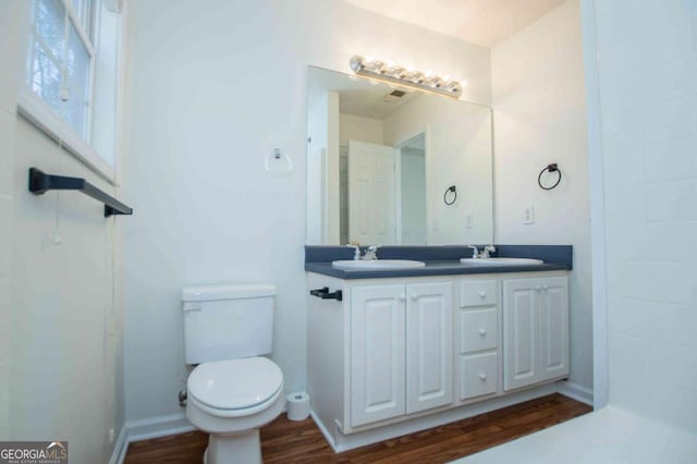 bathroom with toilet, double vanity, a sink, and wood finished floors