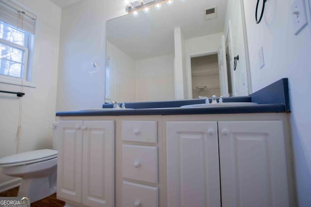 bathroom with toilet, double vanity, a sink, and visible vents