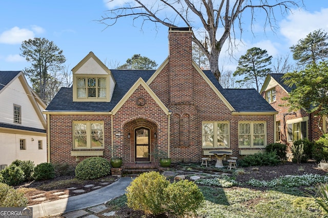 view of front facade with a shingled roof, brick siding, and a chimney