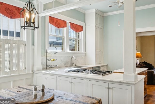 kitchen featuring crown molding, tasteful backsplash, stainless steel gas stovetop, white cabinetry, and a sink