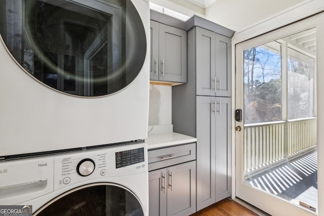 clothes washing area with cabinet space, stacked washer / dryer, and wood finished floors