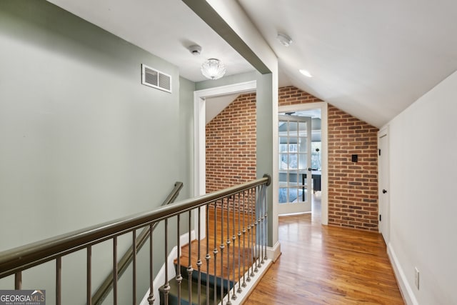 hall featuring visible vents, lofted ceiling, brick wall, wood finished floors, and an upstairs landing