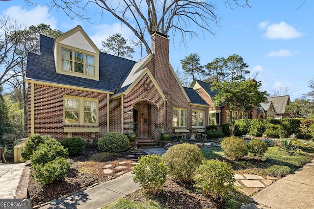 view of front facade featuring roof with shingles, a chimney, and brick siding