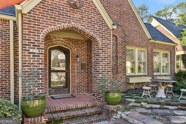 property entrance with a shingled roof and brick siding