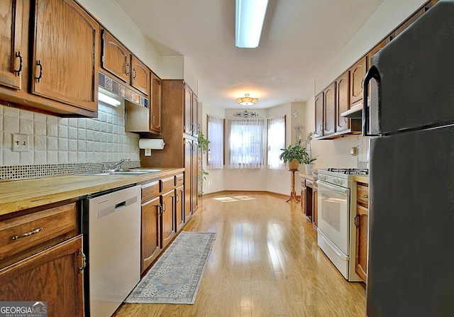 kitchen featuring white range with gas stovetop, dishwasher, freestanding refrigerator, light wood-type flooring, and backsplash