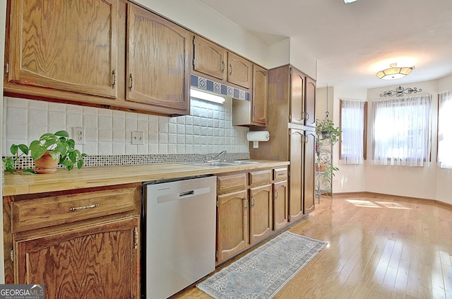 kitchen with a sink, light countertops, light wood-type flooring, backsplash, and dishwasher