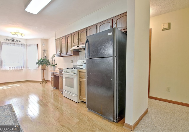 kitchen with light wood finished floors, white range with gas stovetop, baseboards, freestanding refrigerator, and under cabinet range hood