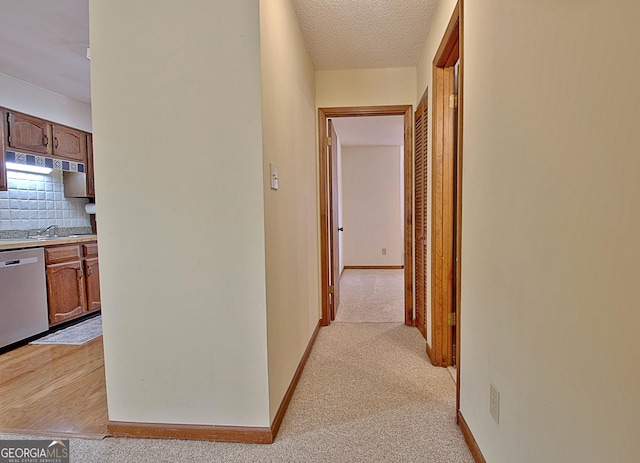 corridor featuring a textured ceiling, a sink, light colored carpet, and baseboards