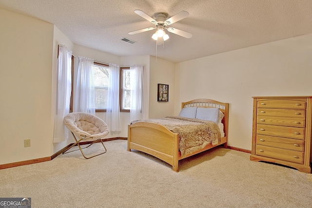 carpeted bedroom featuring baseboards, visible vents, ceiling fan, and a textured ceiling