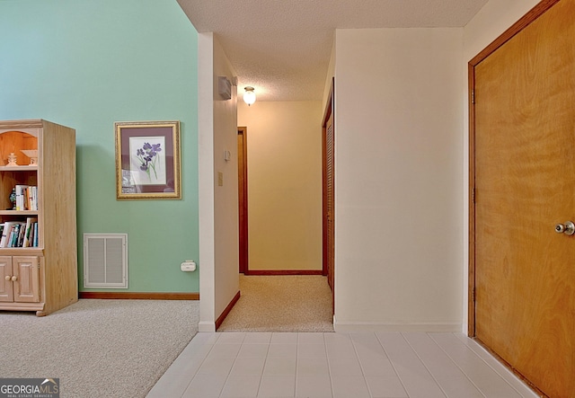 hall with baseboards, visible vents, a textured ceiling, and carpet flooring