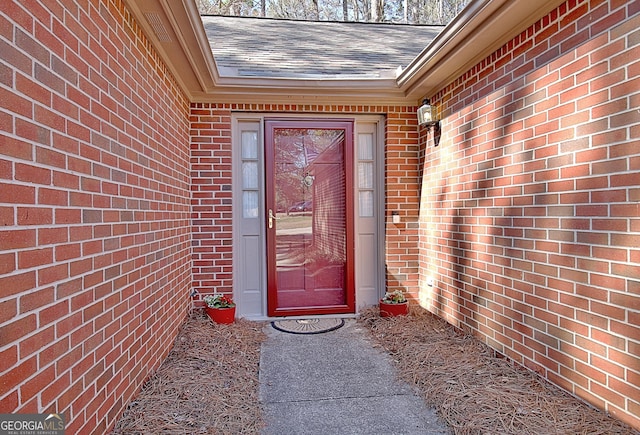 view of exterior entry featuring brick siding and roof with shingles