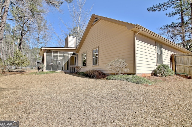 view of side of property featuring a sunroom, fence, and a chimney