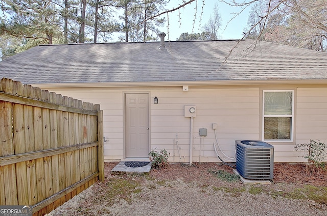 exterior space with central AC unit, a shingled roof, and fence