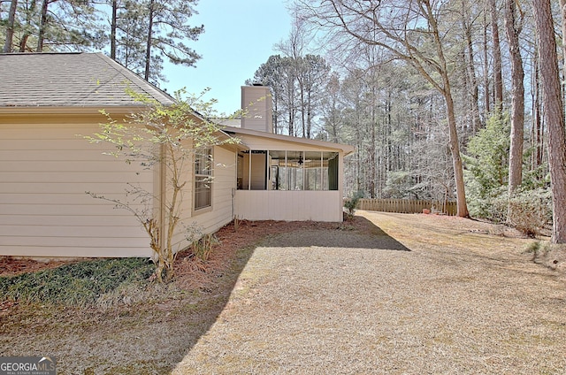 view of side of home with a sunroom, roof with shingles, fence, and a chimney