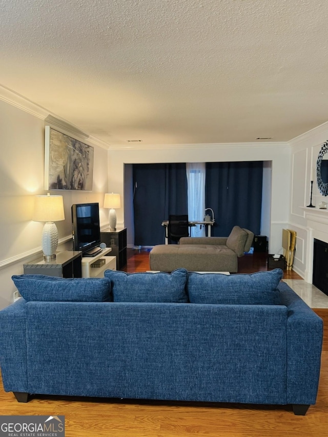 living area with crown molding, a fireplace, a textured ceiling, and wood finished floors