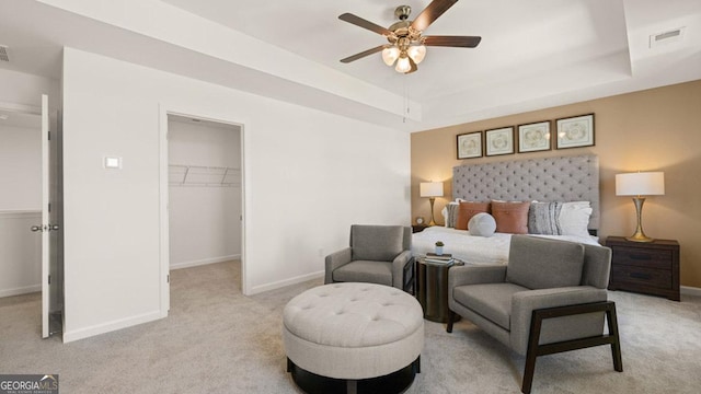 bedroom featuring a walk in closet, a raised ceiling, light colored carpet, visible vents, and baseboards