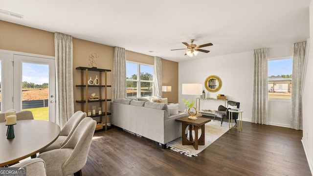 living area with a wealth of natural light, ceiling fan, visible vents, and dark wood-style flooring