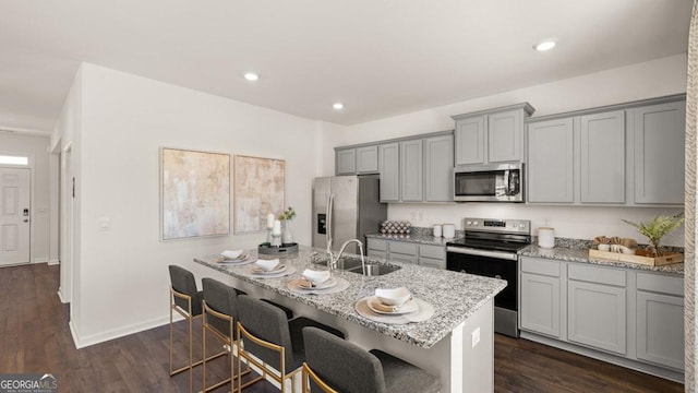 kitchen featuring light stone counters, dark wood-type flooring, gray cabinets, stainless steel appliances, and a sink