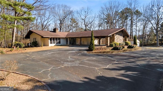 view of front of house with stone siding, aphalt driveway, a chimney, and an attached carport