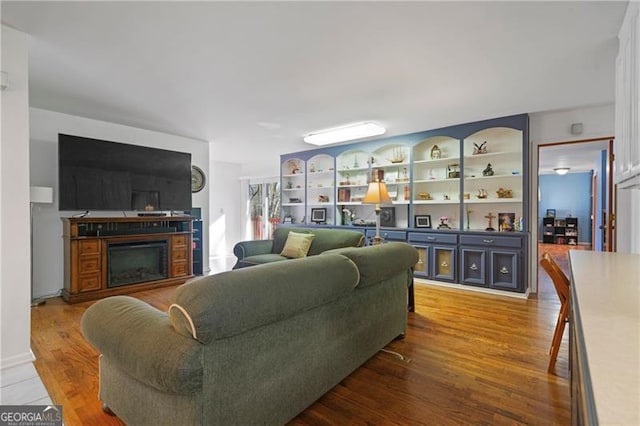 living room with built in features, a fireplace, and wood finished floors