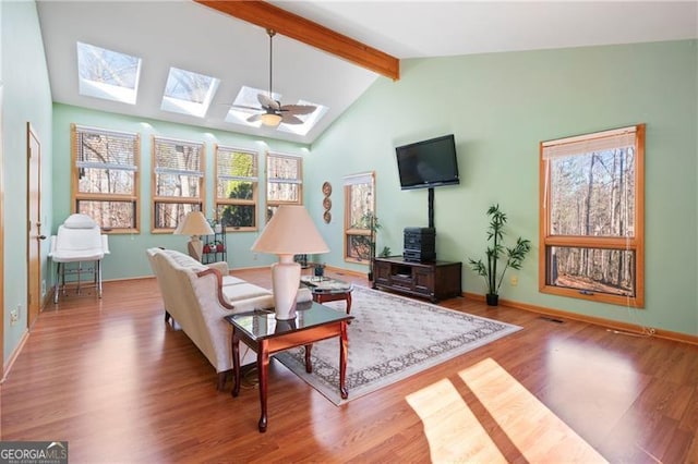 living room featuring vaulted ceiling with skylight, wood finished floors, and baseboards