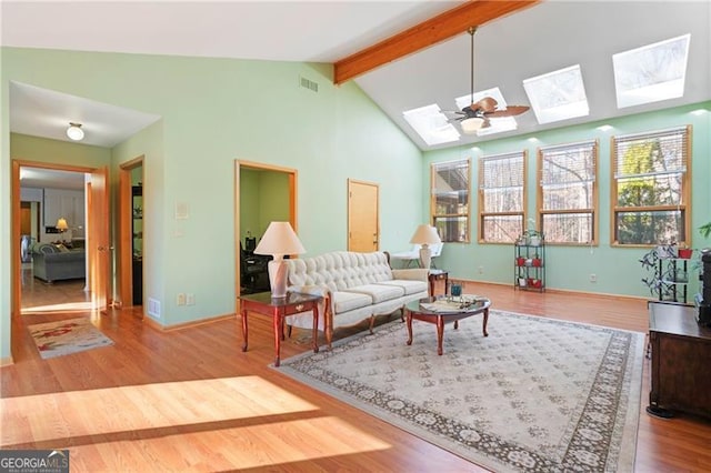 living room with high vaulted ceiling, a skylight, wood finished floors, visible vents, and beamed ceiling