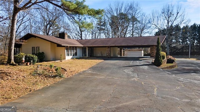 ranch-style house featuring driveway, an attached carport, a chimney, and stucco siding