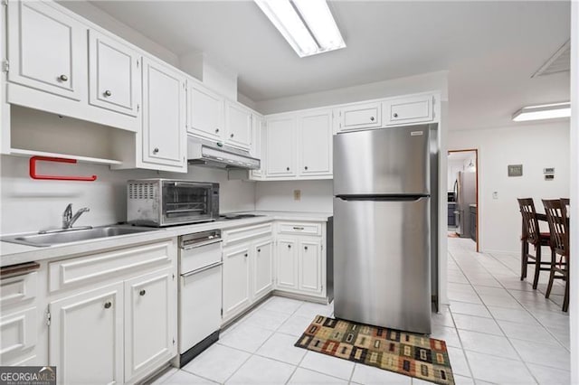 kitchen featuring freestanding refrigerator, a sink, under cabinet range hood, and light tile patterned floors