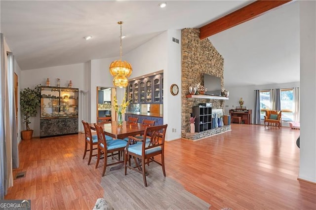 dining space with a fireplace, a notable chandelier, visible vents, wood finished floors, and beamed ceiling