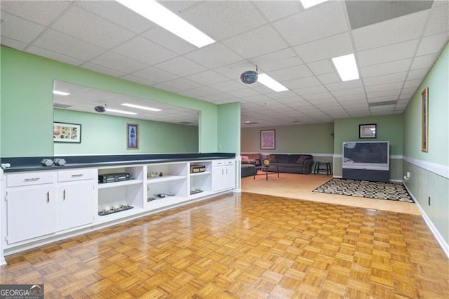 interior space featuring a paneled ceiling and a wainscoted wall