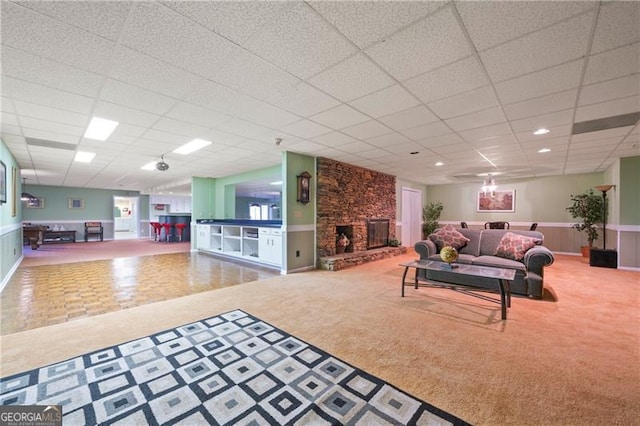 carpeted living area with wainscoting, a drop ceiling, and a fireplace