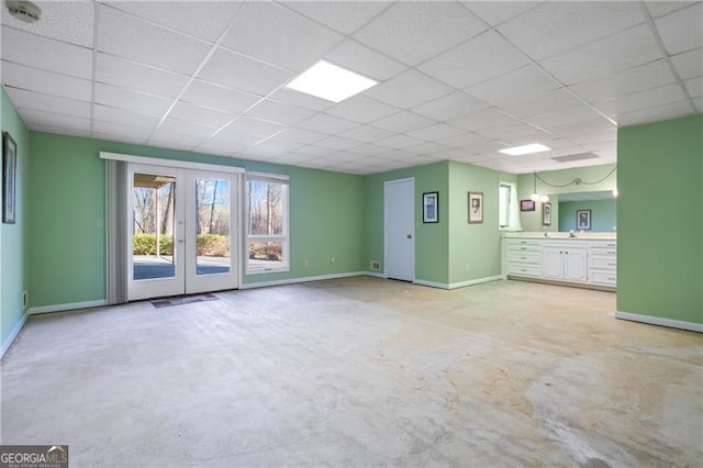 unfurnished living room with unfinished concrete floors, baseboards, a drop ceiling, and french doors