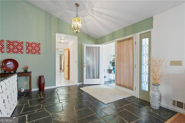 foyer entrance with lofted ceiling, visible vents, a chandelier, and stone tile flooring