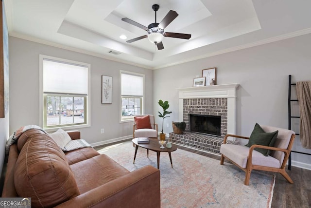 living area with a brick fireplace, baseboards, a tray ceiling, and wood finished floors