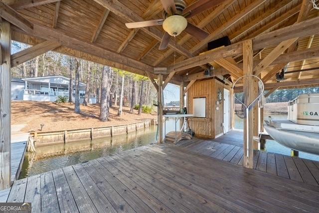 wooden deck featuring a ceiling fan, boat lift, a water view, and a dock