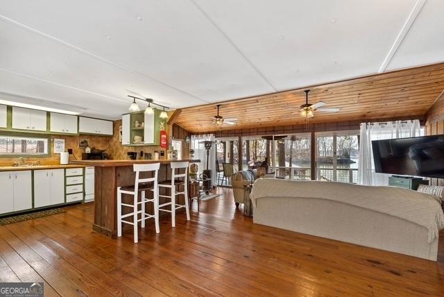 interior space featuring wooden walls, ceiling fan, a breakfast bar, a sink, and hardwood / wood-style floors