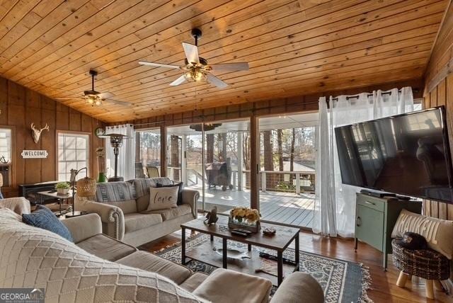 living area with lofted ceiling, ceiling fan, wood walls, wood finished floors, and wooden ceiling