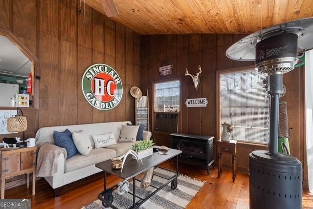 living room featuring plenty of natural light, a wood stove, wood finished floors, and wooden ceiling