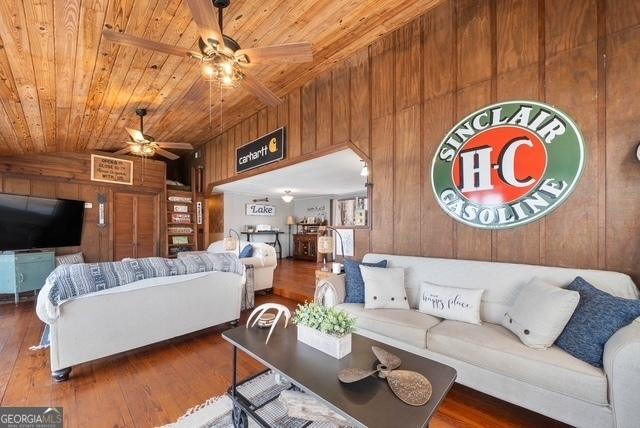 living area with lofted ceiling, wooden ceiling, ceiling fan, hardwood / wood-style floors, and wood walls